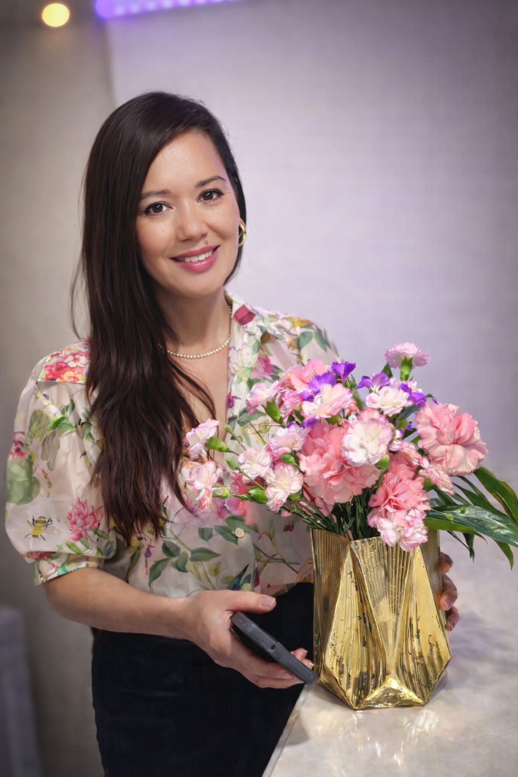 Mia Camille florist holding a gold vase with pink and purple carnations